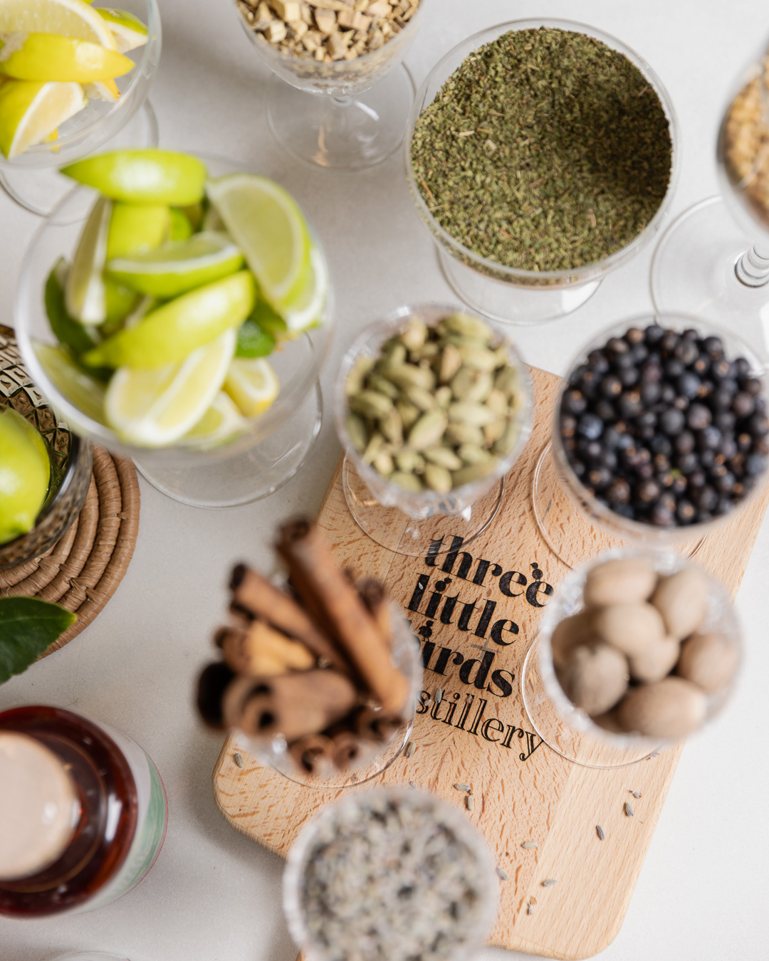 Gin botanicals - juniper, cardamom, cinnamon, nutmeg and citrus - in glasses on a Three Little Birds Distillery board